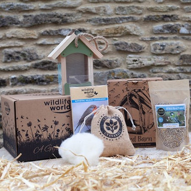 Contents of the For the Love of Birds Gift pack are out of their box infront of a stone wall. The birdhouse is on top of the giftbox, with the wildlife book, the bird seed, the hessien bag and the nesting material arranged in front.