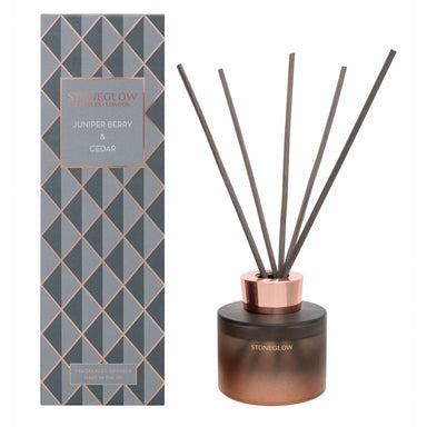 A grey and gold geometric patterned Reed Diffuser box reading Juniper Berry and Cedar. To the right is an image of the diffuser, a copper and grey coloured glass base with five diffuser sticks.