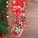 A stocking full of dog treats and a rope toy. The stocking is on a wooden floor with pine branches, berries and baubles on the side.