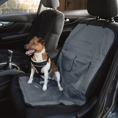 A small dog is sat on a single car seat protector inside a car.