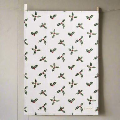 A white tea towel decorated with a repeating pattern of holly and berries.