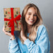 A woman holding a wrapped present. The wrap is brown with illustrations of candy canes and festive presents.