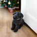 a Black Labrador doorstop in front of a white door. There is a Christmas tree in the background.