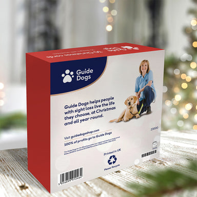 Back of the red box containing 30 assorted Christmas cards on a wooden table with Christmas tree and lights in the background.