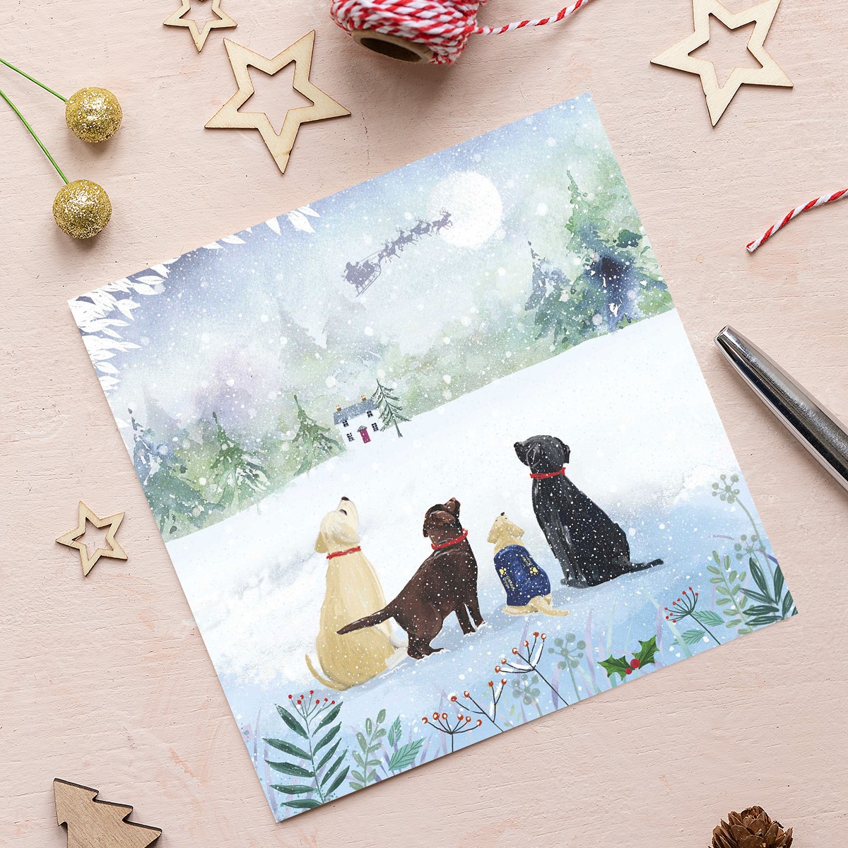 A Christmas card featuring four Labradors sitting in the snow watching Father Christmas's sleigh cross the moon.