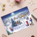 A Christmas card featuring a village covered in snow with its residents singing, sledging and building snowmen. A Guide Dog owner puts a parcel into the postbox.