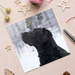 A Christmas card featuring a black Labrador sitting perfectly while snow falls all around.