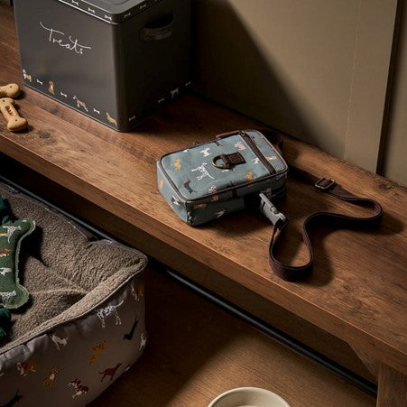 A rectangular bag printed in dog pattern with brown trims and webbing strap, on a wooden bench