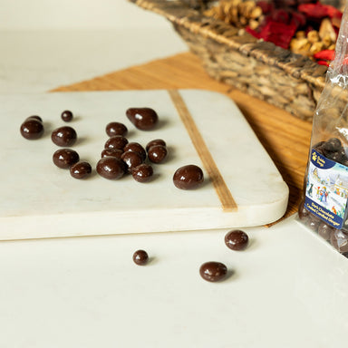 A photograph of a selection of dark chocolate candied ginger pieces. The clear bag packaging can be seen in the background.