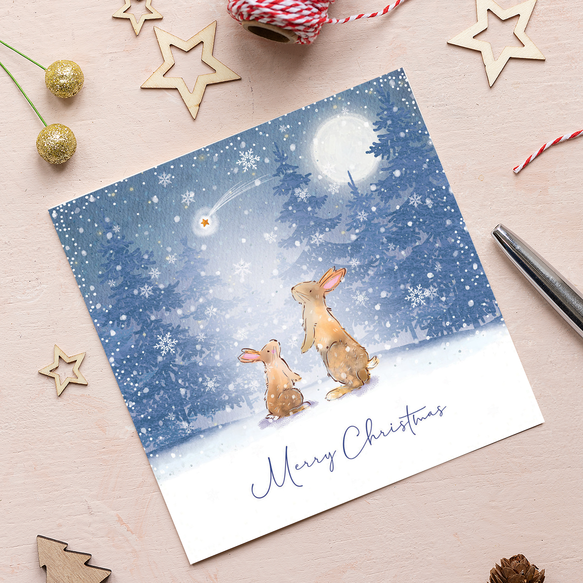 An illustrated Christmas card featuring two rabbits watching a shooting star. The background is a snowy forest with the words 'Merry Christmas' at the bottom.