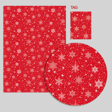 A close-up of a piece of wrapping paper and tag. The wrap is red with white snowflakes and stars.