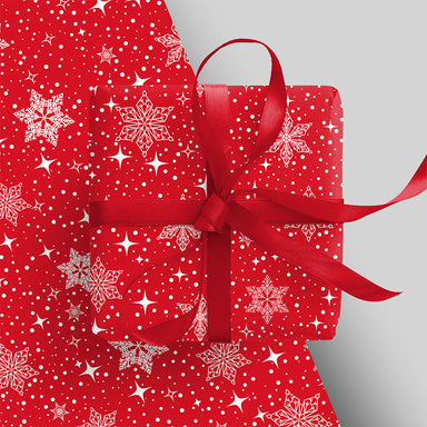 A piece of wrapping paper appears underneath an already wrapped present with red ribbon. The wrap is red with white snowflakes and stars.