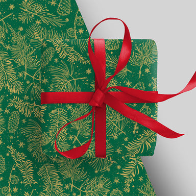 A piece of wrapping paper appears underneath an already wrapped present with red ribbon. The wrap is green with an illustration of gold leaves and tiny stars.