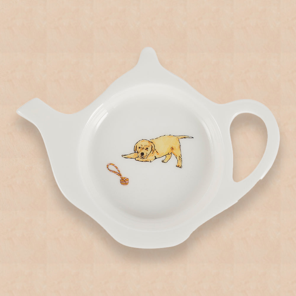 A white china teabag tidy in the shape of a teapot, with Labrador puppy and rope toy design on a peach background.