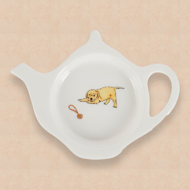 A white china teabag tidy in the shape of a teapot, with Labrador puppy and rope toy design on a peach background.