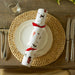 A cracker with Christmas dogs pattern and red ribbons placed on a wooden table with cutlery.