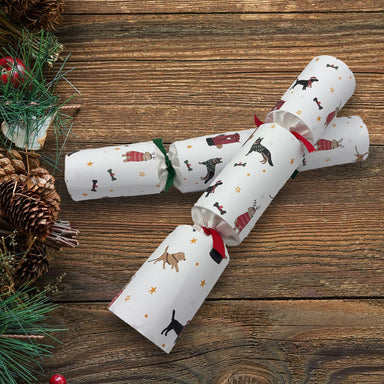 Two crackers with Christmas dogs pattern and red and green ribbons placed on a wooden table, with pine cones at the side