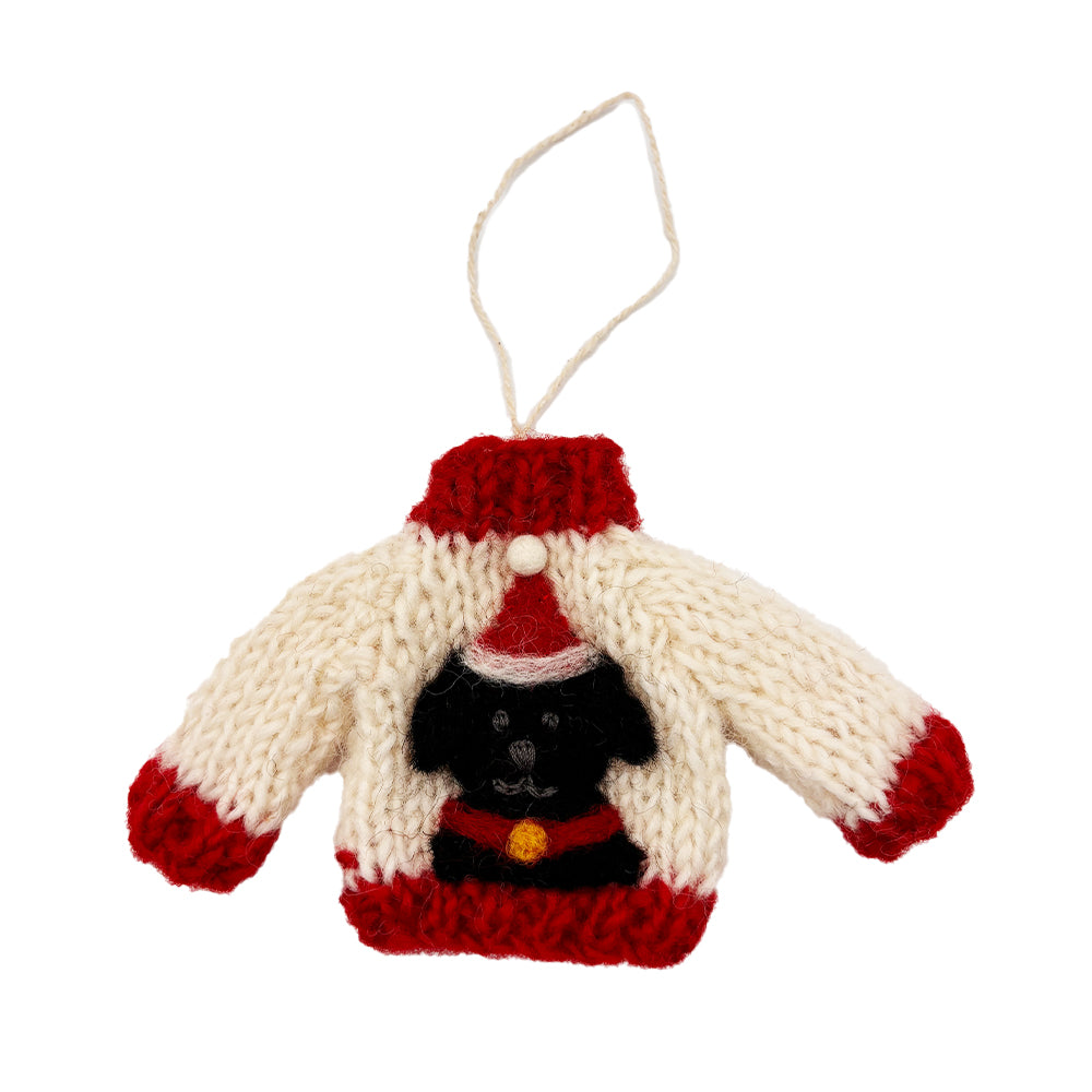 A white knitted decoration with red edges, in the shape of a jumper. It features a black Labrador wearing a Santa hat.