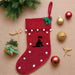 A red felt Christmas stocking with a black Labrador design, on the floor with Christmas decorations around it.