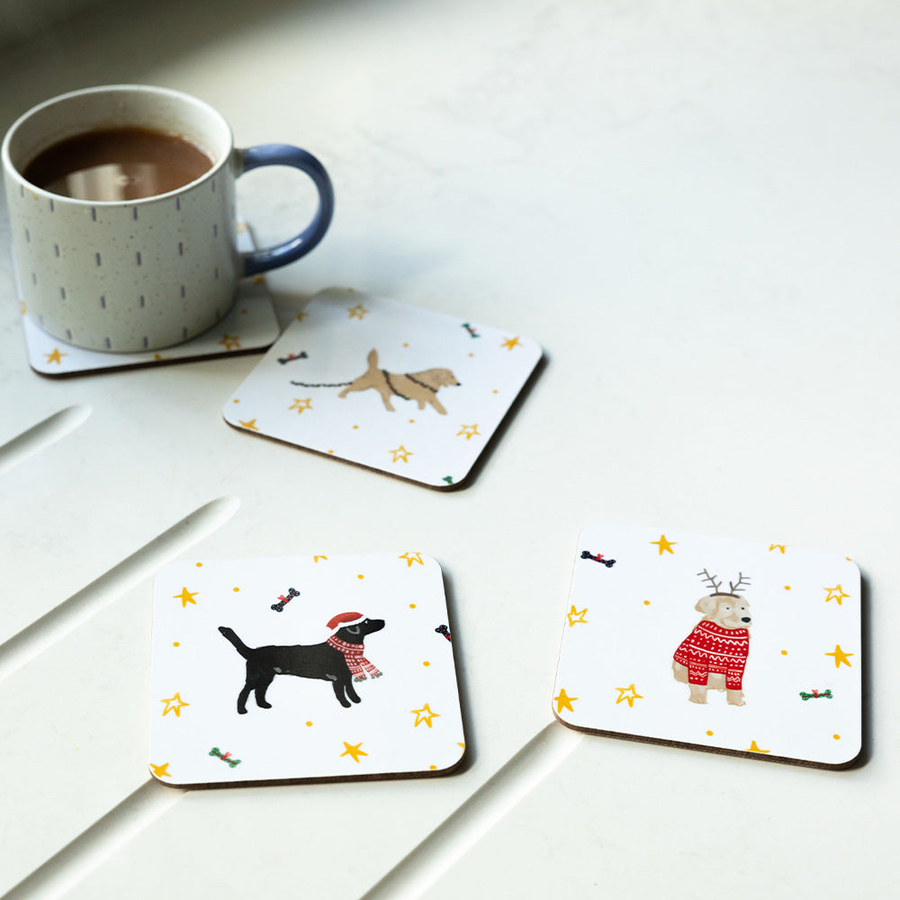 Four coasters on a counter top. Each coaster features a different festive dog: German Shepherd, Yellow Labrador, Golden Retriever and Black Labrador. The German Shepherd is covered by a stoneware mug.