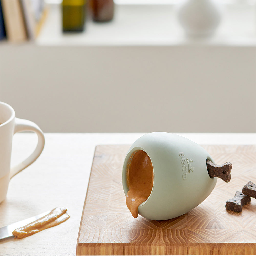 A green rubber toy filled with treats and peanut butter on a kitchen counter.