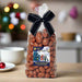 A packet of milk chocolate covered honeycomb bites in a clear bag with a black ribbon and a sticker on the front featuring an illustration of a Christmas village scene.