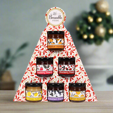 Six mini jars of preserves presented in packaging the shape of a Christmas tree.