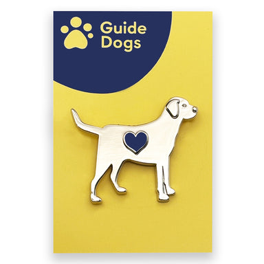 A silver metal pin badge in the shape of a Labrador with a blue heart in the centre. The pin is on a Guide Dogs logo backing card.