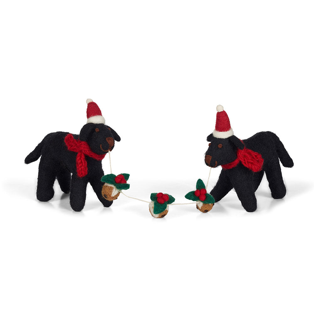 2 felt Labradors with red scarfs and Santa hats hold a string of 3 Christmas puddings on a white background