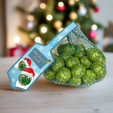 Chocolate sprouts in a green net bag with a blue label, on a table with Christmas decorations in the background.