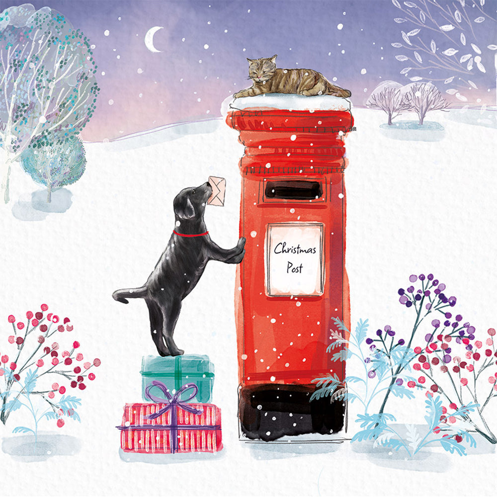 An illustration of a Black Labrador puppy with a letter in its mouth, trying to reach a red post box. The puppy is in the snow, stood on some presents to give extra height. A cat is laying on top of the post box.