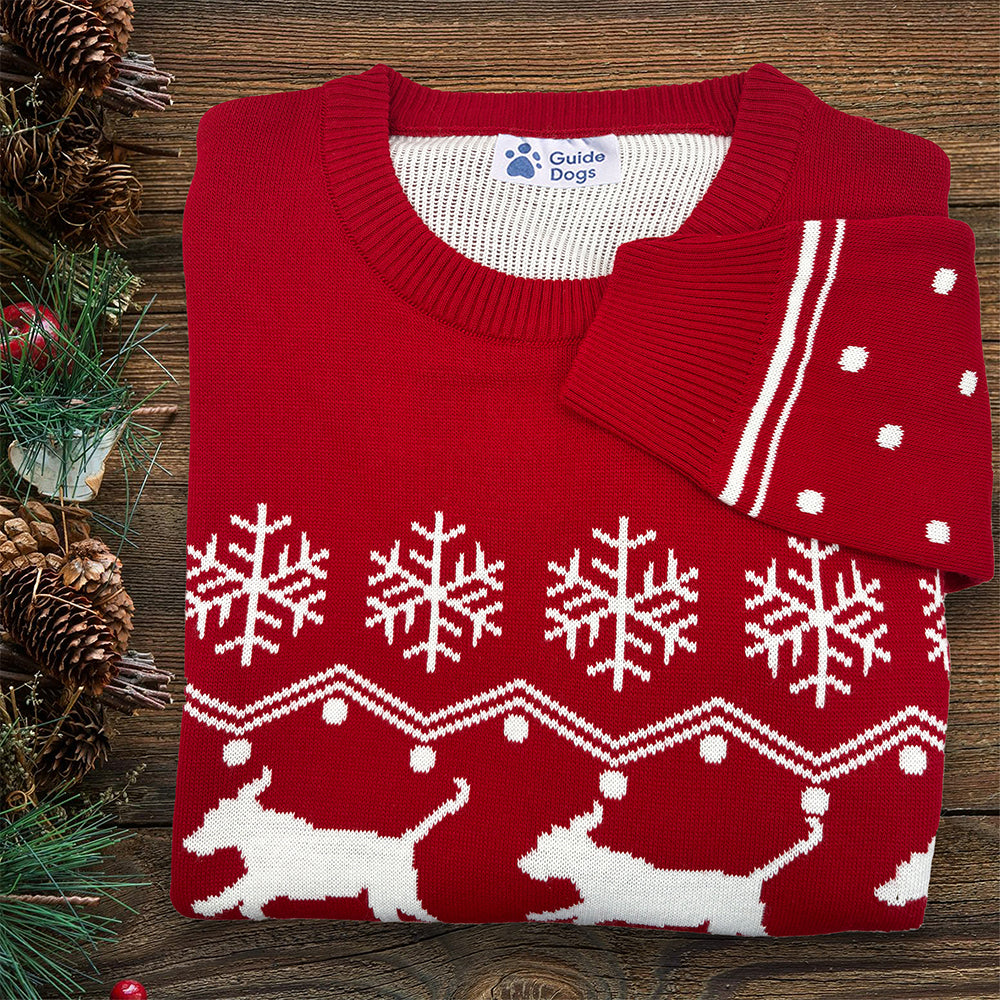 A folded red and white jumper on a wooden background, with Guide Dogs inner neck logo label visible.