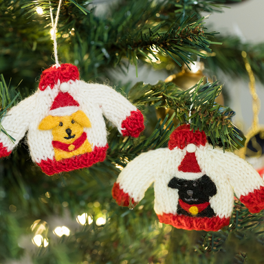 Two knitted Christmas jumper decorations, one featuring a black Labrador, the other a golden Labrador. Both jumpers are white with red edges and the Labradors are wearing a Santa hat. 