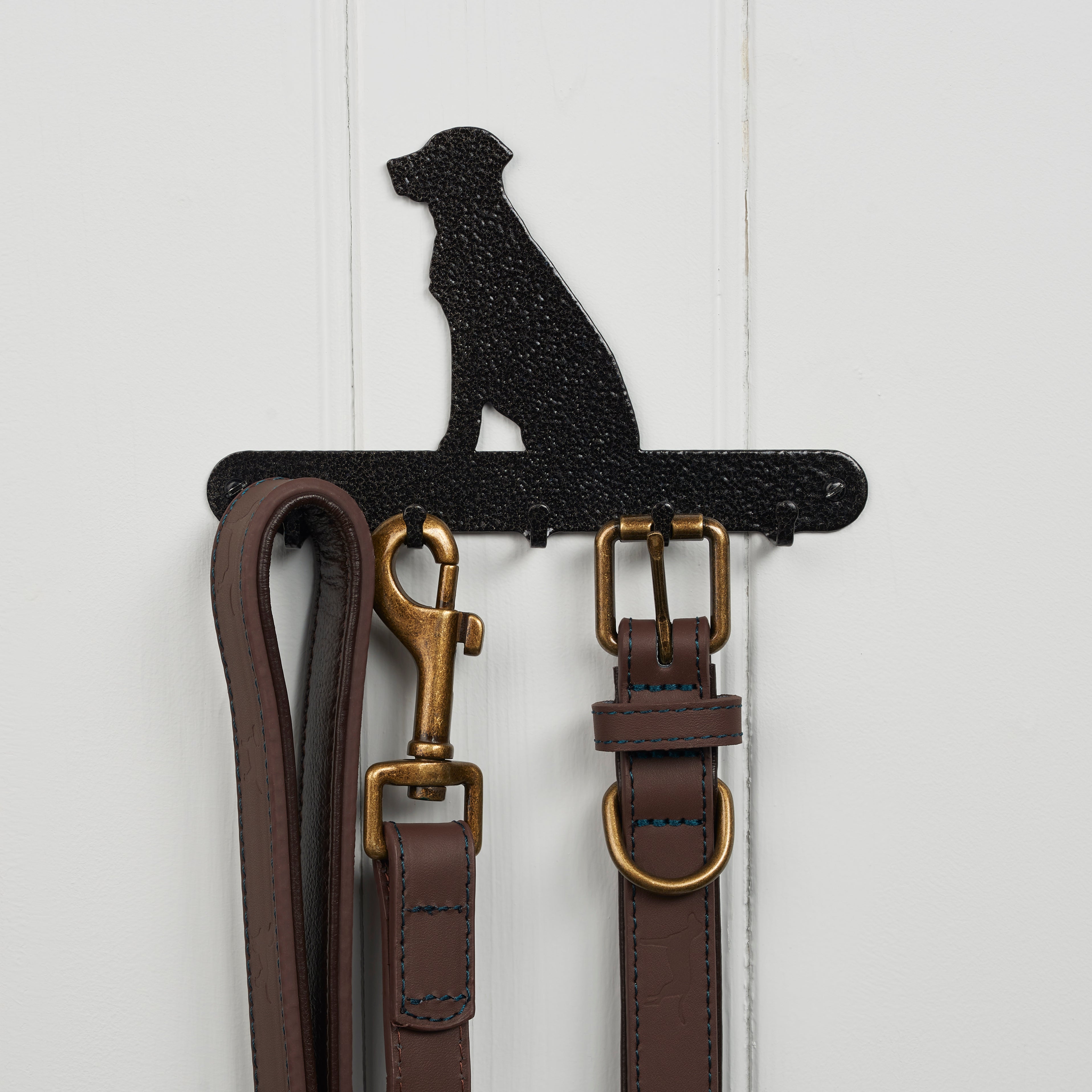 A black silhouetted Labrador lead holder is fixed to a wall, with leather leads and collars hanging from it