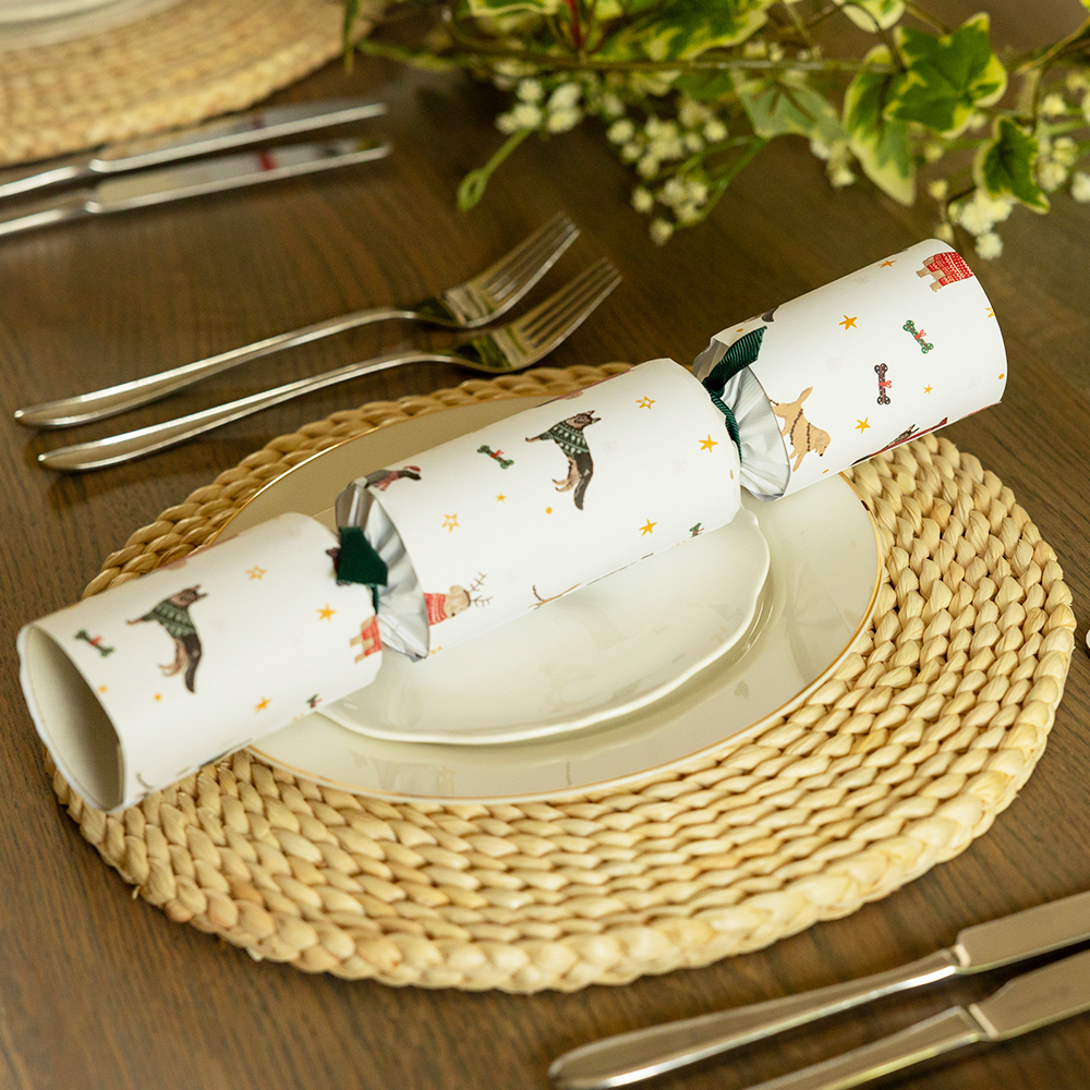 A cracker with Christmas dogs pattern and green ribbons placed on a wooden table with plates and cutlery.