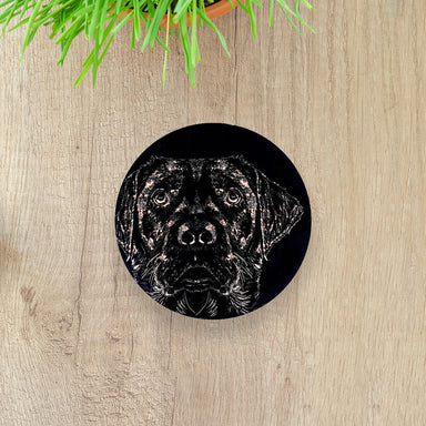 A round slate magnet with Labrador head engraving. On a wooden table background.