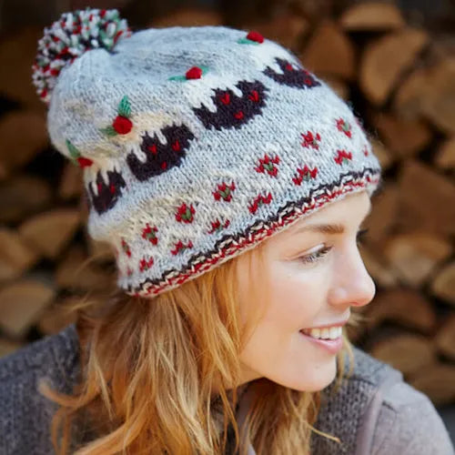 A woman wearing a light grey woolly bobble hat with Christmas pudding pattern and multicoloured bobble on top.