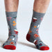 Man's lower legs wearing grey socks with Christmas pattern including holly and gingerbread men