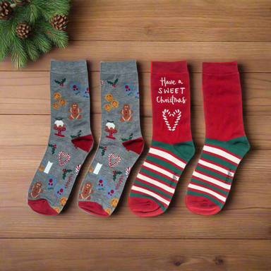 Two pairs of Christmas socks on a wooden background. One pair has a seasonal pattern on a grey background, the other a classic red and green stripe.