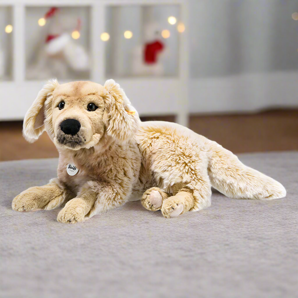 A soft toy golden retriever lying down, with a Steiff branded dog tag on the collar.