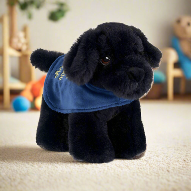 A small Black Labrador soft toy wearing a blue Guide Dogs coat.