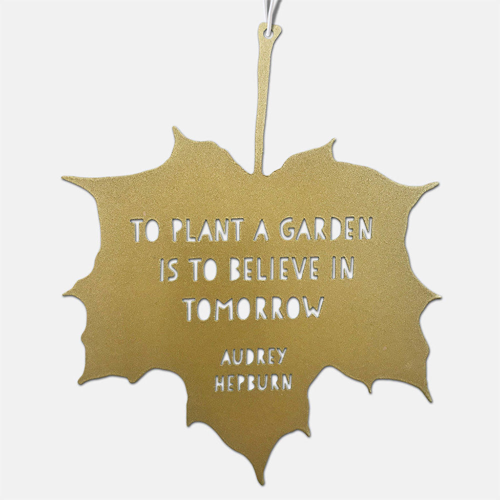 A gold hanging leaf with the quote 'to plant a garden is to believe in tomorrow'. Audrey Hepburn's name appears below. 
