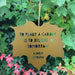 A gold hanging leaf with the quote 'to plant a garden is to believe in tomorrow'. Audrey Hepburn's name appears below.  The background features lots of leaves.