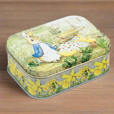 A tin featuring an illustration of Peter Rabbit and an Easter scene. The tin is on a wooden background.