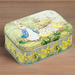 A tin featuring an illustration of Peter Rabbit and an Easter scene. The tin is on a wooden background.