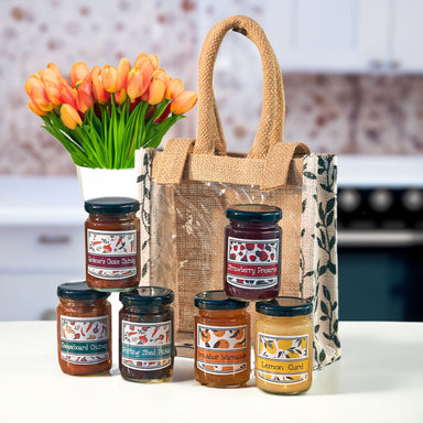 An image of a jute bag with chutney and preserves stacked on a kitchen table.