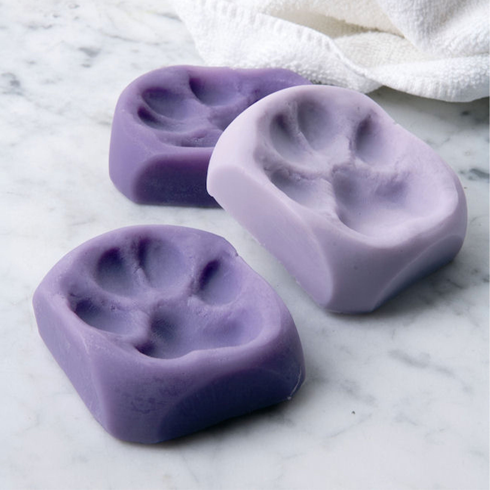 Three pawprint lavender soap bars on a white marble surface.