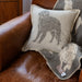A cream wool cushion with Labrador in grey design sits on a brown leather armchair