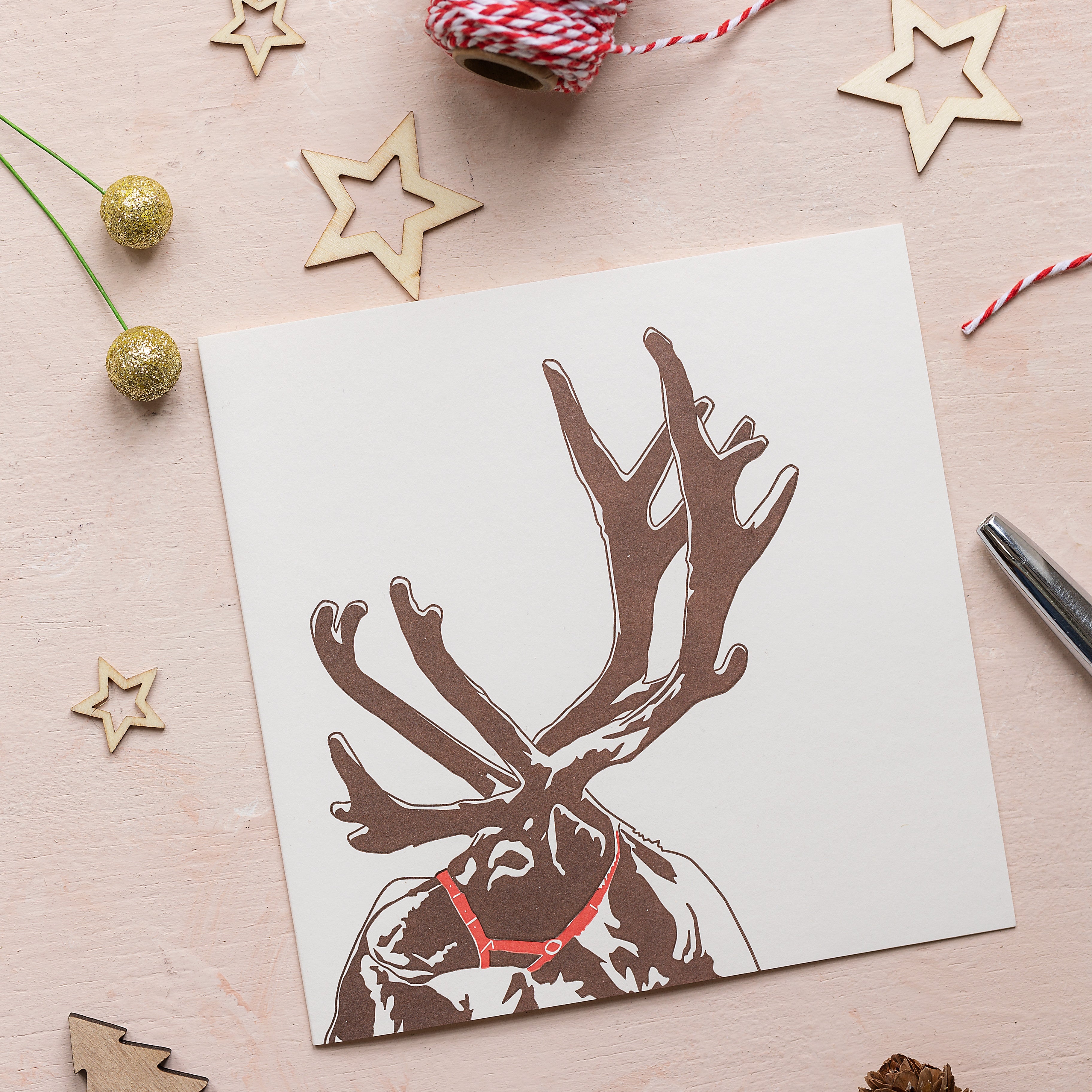 A white card with brown reindeer head and antlers sits on a table scattered with gold Christmas stars