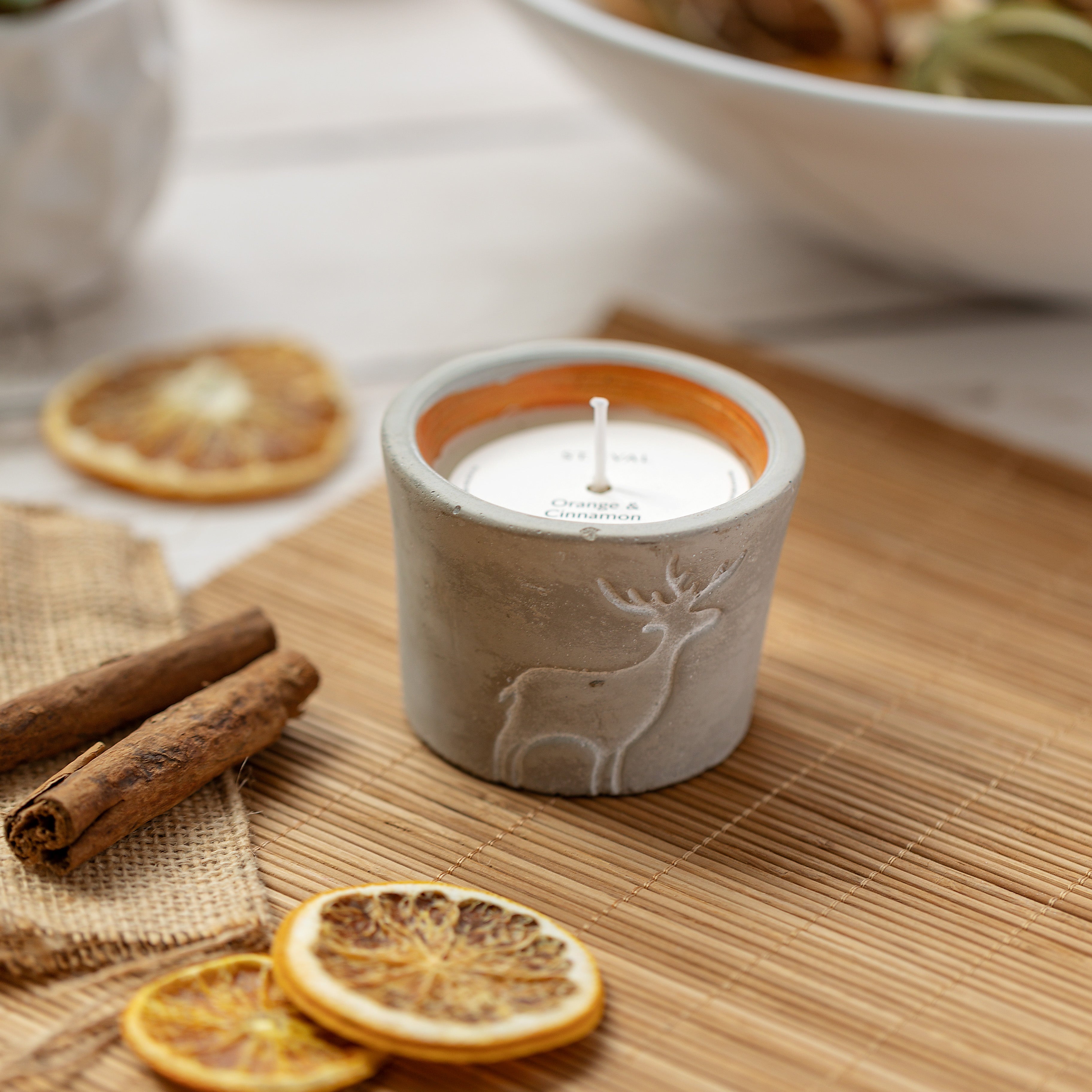 A grey candle pot with etched reindeer design on a Christmas table with dried orange slices and cinnamon sticks